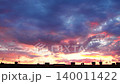 A beautiful sunset displays colorful clouds over a city skyline. The bright colors fill the sky as the sun sets behind buildings. This moment captures the changing light of dusk 140011422