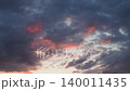 Clouds move slowly in the sky as the sun sets over the ocean. Bright colors fill the sky with shades of orange and pink. The calm evening shows the beauty of nature 140011435