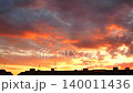 Bright colors fill the sky as the sun sets behind the city buildings. Dark clouds gather and the light shifts, creating a changing view. This captures the beauty of nature at dusk 140011436