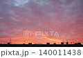 Colors fill the sky as the sun sets behind city buildings and electric poles. The sky changes with shades of orange and pink as evening arrives and night begins 140011438