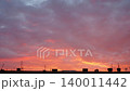 Bright colors fill the sky as day turns to night. The city skyline stands dark against the warm hues of orange, pink, and purple clouds. Evening light creates striking shadows 140011442