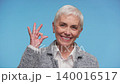 Smiling senior woman showing OK hand sign on blue 140016517