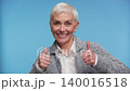 Smiling senior woman showing thumbs up on blue 140016518
