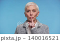 Senior woman making silence gesture in studio 140016521