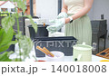 Woman adds dark potting soil with trowel from black bucket while preparing planter. Concept of repotting and container gardening 140018008