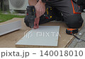 Man drills hole in furniture panel on cardboard outside. Concept of furniture assembly, DIY repair and installation 140018010