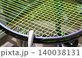 Tennis racket being restrung with bright green tennis strings on stringing machine, hands using metal clamp tool. Tension of string during the stringing process. Regular maintenance of sports gear 140038131