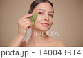 Young woman doing massage facial skin with jade gua sha scraper 140043914