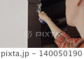 Woman paints dark door frame with small roller beside light wall. Concept of DIY renovation, repair and interior painting 140050190