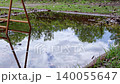 Clouds and blue sky reflected in a puddle; the water's surface swaying in the wind; sweetgum fruit; reflection; live-action; fixed shot. 140055647