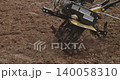 Close-up of a rotary cultivator tilling the soil, preparing the land for planting seeds in a garden. The machine's blades spin, digging into the earth and turning it over for farming work. 140058310