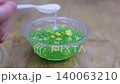 Traditional Thai dessert sago with corn and coconut milk being poured from a spoon into a glass bowl on wooden background. Sweet tapioca pearls with coconut cream topping and jelly texture. 140063210