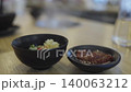 Small black ceramic bowls containing minced garlic and spicy red chili paste condiments on a wooden restaurant table. Close-up shot with shallow depth of field and soft background bokeh. 140063212