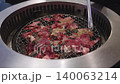 Thin slices of raw beef grilling on a traditional round wire mesh charcoal barbecue. Metal tongs handle the meat over hot coals. Authentic Japanese yakiniku or Korean BBQ dining experience. 140063214