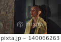 Woman in sports bra stands in front of dark lockers with yellow towel around her neck and hands on her head after intense physical workout 140066263