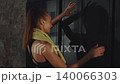 Fit woman with ponytail and towel around neck stands near locker in gym changing room after workout, sporty healthy lifestyle moment 140066303