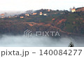 Village mosque and minaret rise above hillside homes in Turkey beneath misty mountain cloud. Historic tower and rural settlement create a cultural landscape with heritage, fog, and quiet life. 140084277