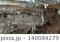Stalactite ceiling reveals fractured limestone inside a cavern with rich mineral structure. Rock formations and brown calcite texture create an underground geology scene with rugged detail. 140084279