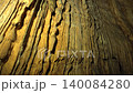 Limestone stalactites hang inside a cave, showing karst formations and underground texture. Dripstone structure and lit chamber create a subterranean scene with natural detail. 140084280