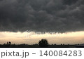 Storm clouds gather over flat grassland at dawn, darkening the plain before rainfall. Grey sky and incoming weather front create a tense rural scene with open field exposure. 140084283