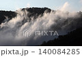 Sunrise light enters a misty valley, illuminating mountain ridges and soft morning fog. Golden dawn and humid air create a tranquil upland scene with atmospheric countryside depth. 140084285