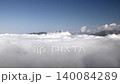 Sunlight reaches distant mountain peaks while white clouds drift across a clear highland sky. Open range and airy atmosphere create an elevated panorama with bright weather and broad vista. 140084289