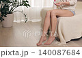 Beautiful woman sitting on the bed at home, applying body lotion and moisturizing cream on her smooth legs for skin care and wellness 140087684