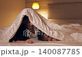 Young, happy mother and her little daughter playing together in bed. Playful family having fun under a duvet in a cozy bedroom at night 140087785