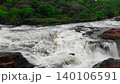 Powerful whitewater waterfall rushing through dark rocks in a lush green forest landscape . Media 140106591