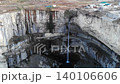 Aerial view of a rocky open-pit quarry with waterfall and dark basin . Media 140106606