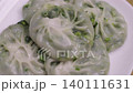 Close-up shot of steamed Chinese chive dumplings with translucent dough and green vegetable filling. Traditional Asian dim sum snacks served on a white plate. 140111631