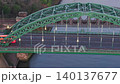 Aerial telephoto tracking shot moving sideways alongside the Wearmouth Bridge in Sunderland at dawn, featuring early morning traffic and the Monkwearmouth Railway Bridge in the background. 140137677