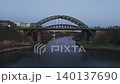 Aerial drone shot flying upwards and backwards from the Wearmouth Bridge and Monkwearmouth Railway Bridge in Sunderland at dawn, revealing the river and city buildings in twilight. 140137690