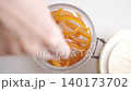 Hand places candied orange peel into glass jar. Concept of homemade citrus candy and food storage 140173702