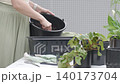 Woman scoops dark soil with small trowel beside planter box and potted plants. Concept of repotting, container gardening and plant care 140173704