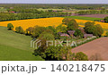 Aerial drone view of a traditional farmstead among green trees, bordered by vibrant yellow rapeseed fields, plowed earth, and green pastures in the countryside. 140218475