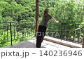 A slender woman doing push-ups on a balcony railing. A female version of a high-handle push-up against a backdrop of green trees swaying in the wind 140236946