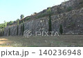 A beautiful high stone wall along which thuja trees grow. Green grass grows near the wall. View from right to left. Rest stop on the highway 140236948
