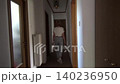 A slender woman with her hair pulled back walks down a long hallway and approaches a closed door. The blonde is wearing blue jeans and a light-colored short-sleeved T-shirt 140236950