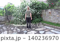 A girl rises on her toes while performing an exercise to improve blood circulation against the backdrop of a lush bush with white flowers 140236970