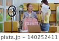 Two asian woman live streaming online clothing store while showing clothing with smartphone on social. 140252411