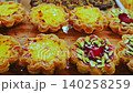 Colorful pastry tarts with creamy custard and fruit toppings are arranged on a wooden display, highlighting their textures and vibrant colors in a bakery setting 140258259