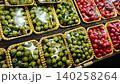 Green olives and red cherry tomatoes neatly packaged in transparent containers, displayed attractively at a market, inviting customers to purchase fresh produce 140258264