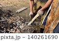 A man carves and shapes a wooden block to make a support leg for a tall raised garden bed 140261690