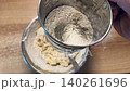 A man hand holds a mechanical flour sifter and sifts flour into dough during the baking process 140261696