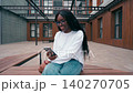 Young woman sits outside and uses smartphone in urban setting during daytime 140270705