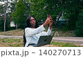 Young woman takes selfie while sitting outside with laptop during daytime 140270713