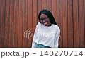 Smiling woman stands in front of wood wall at outdoor location during daytime at a casual setting 140270714