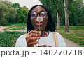 Woman smiles while holding a dandelion in a park in springtime with trees and grass around her 140270718