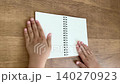 一段4K無聲視頻，從對角線角度拍攝，畫面中一個孩子的手撫平並拉直了一本小型活頁筆記本的左側頁面。 140270923